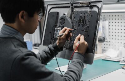 A technician works on a computer motherboard using tools at a workspace, focusing on electronics repair.