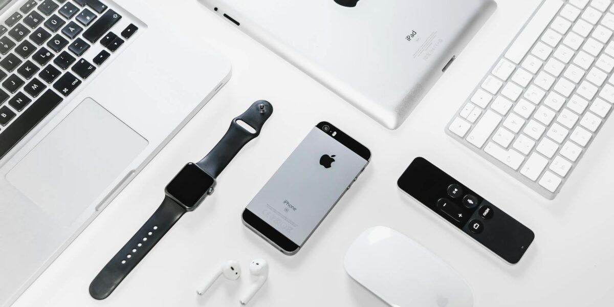 Flat lay of Apple devices including iPhone, iPad, MacBook, and Watch on a white surface, ideal for tech enthusiasts.