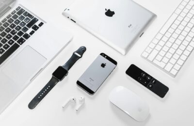 Flat lay of Apple devices including iPhone, iPad, MacBook, and Watch on a white surface, ideal for tech enthusiasts.