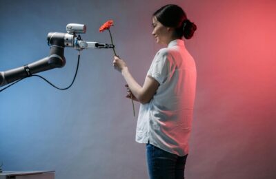 A woman interacts with a robotic arm holding a flower, showcasing technology and human connection.