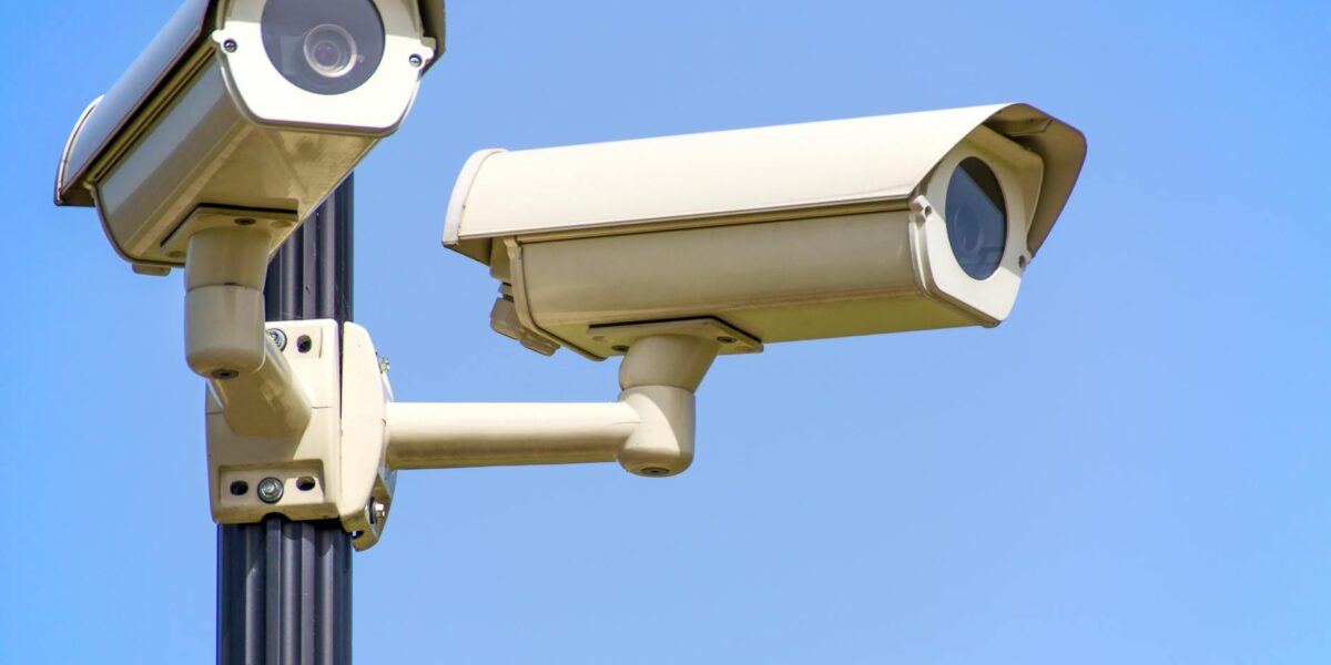 Outdoor security cameras mounted on a pole against a clear blue sky, ensuring vigilant surveillance.