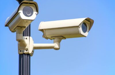 Outdoor security cameras mounted on a pole against a clear blue sky, ensuring vigilant surveillance.