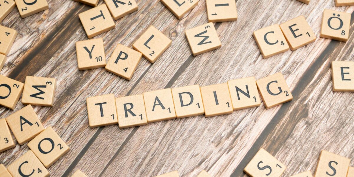 Wooden Scrabble tiles spelling 'TRADING' against a rustic wood background.