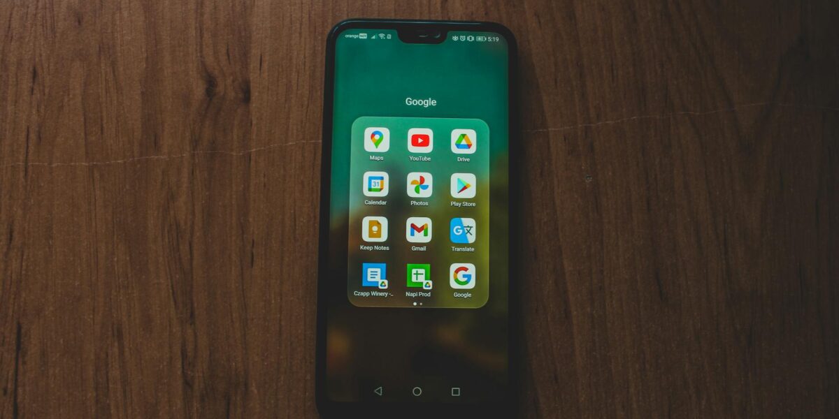 A smartphone showcasing various Google apps on a wooden table.