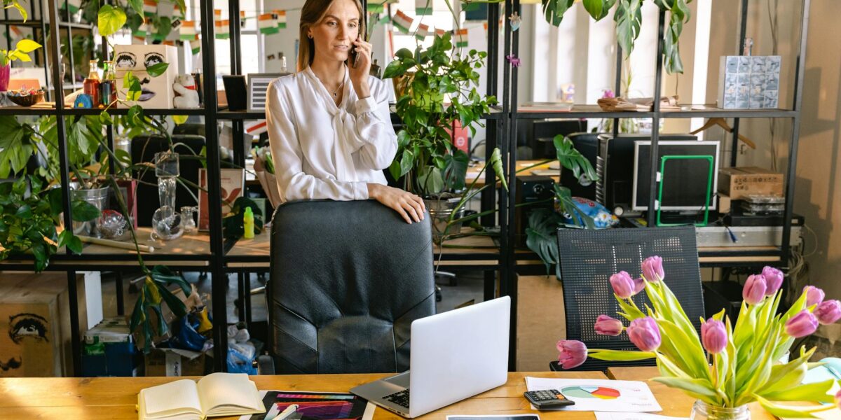 Professional woman on phone in a stylish office, surrounded by greenery and technology.