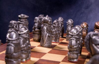 Intricate medieval-themed chess pieces set on a classic wooden board with a dramatic backdrop.