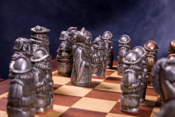 Intricate medieval-themed chess pieces set on a classic wooden board with a dramatic backdrop.