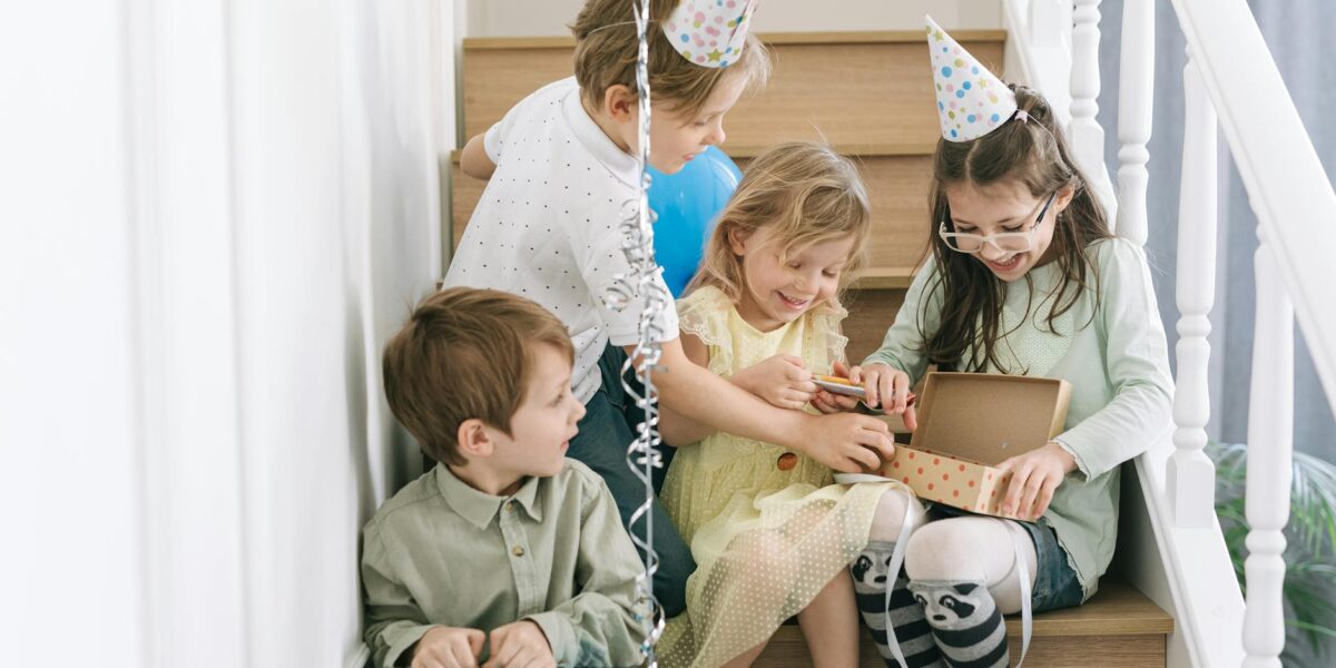 Children enjoying a birthday party with gifts and balloons, captured indoors on a staircase.