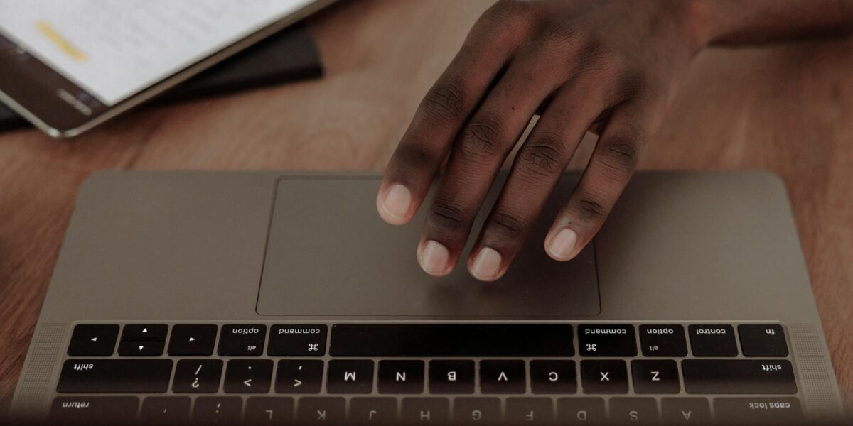 A person's hand interacts with a laptop touchpad beside a tablet with documents.