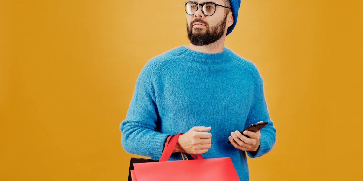 Stylish man in blue holding sale bags and smartphone, looking away.