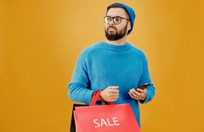 Stylish man in blue holding sale bags and smartphone, looking away.