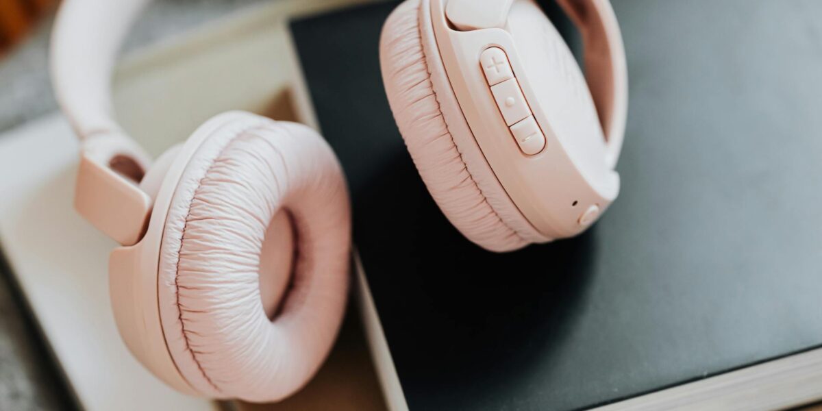 Soft pink wireless headphones placed on stacked books, ideal for music enthusiasts.