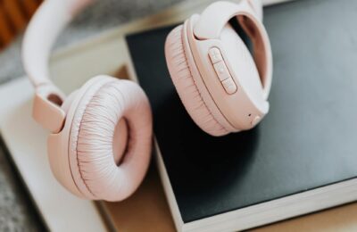 Soft pink wireless headphones placed on stacked books, ideal for music enthusiasts.