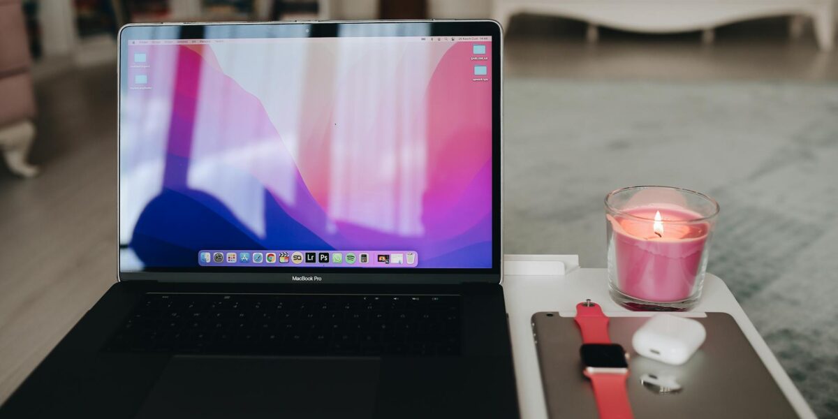 A modern workspace setup featuring a laptop, candle, AirPods, and Apple Watch.