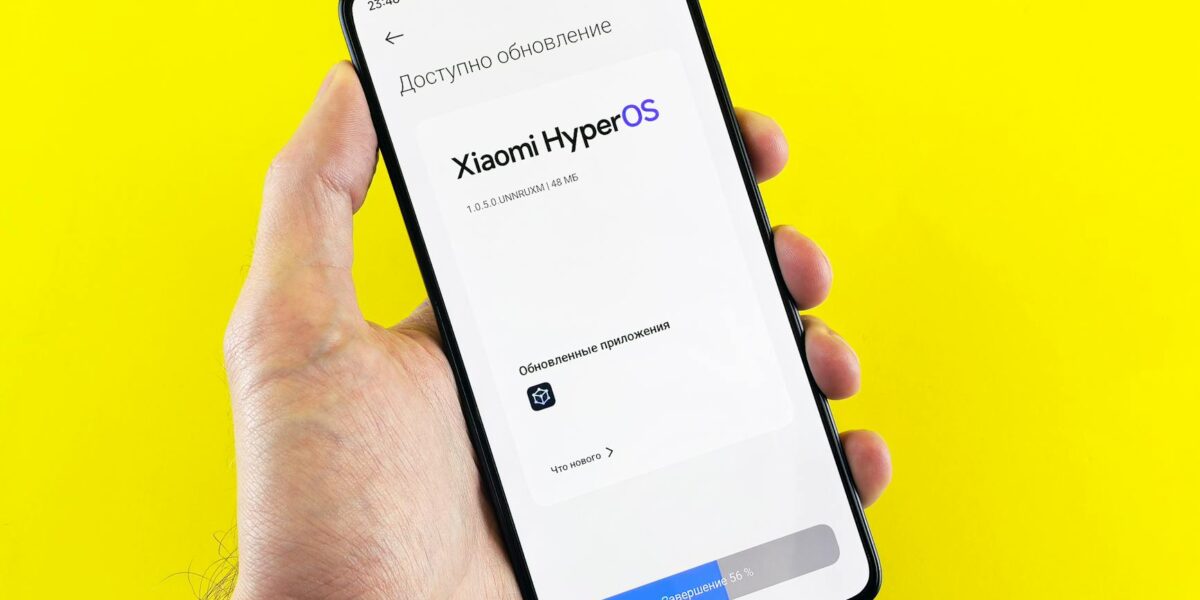 Hand holding smartphone showing Xiaomi HyperOS update screen on yellow background.