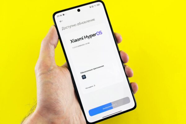 Hand holding smartphone showing Xiaomi HyperOS update screen on yellow background.