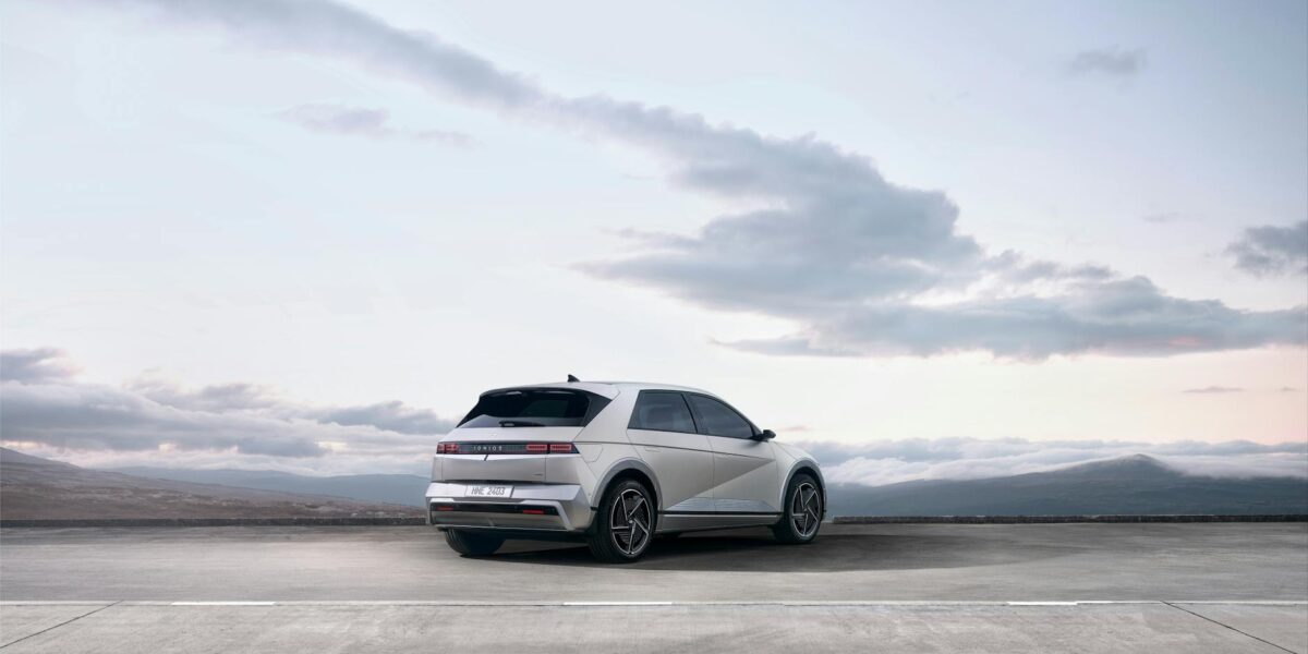 A sleek white electric SUV parked on an open road with a scenic backdrop of mountains and sky.