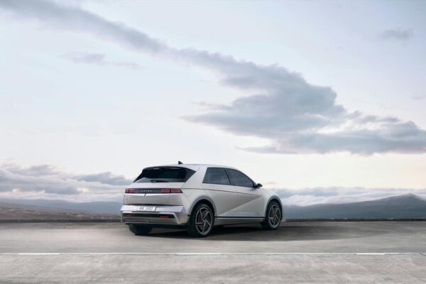 A sleek white electric SUV parked on an open road with a scenic backdrop of mountains and sky.