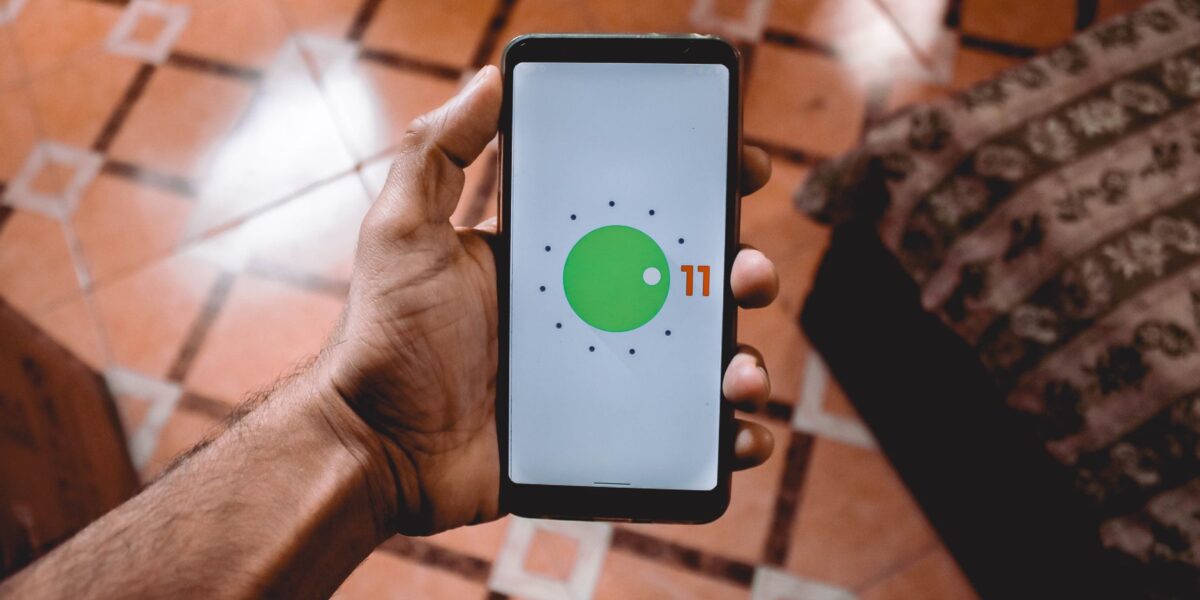 Close-up of a hand holding a smartphone displaying Android 11 interface indoors on patterned floor.