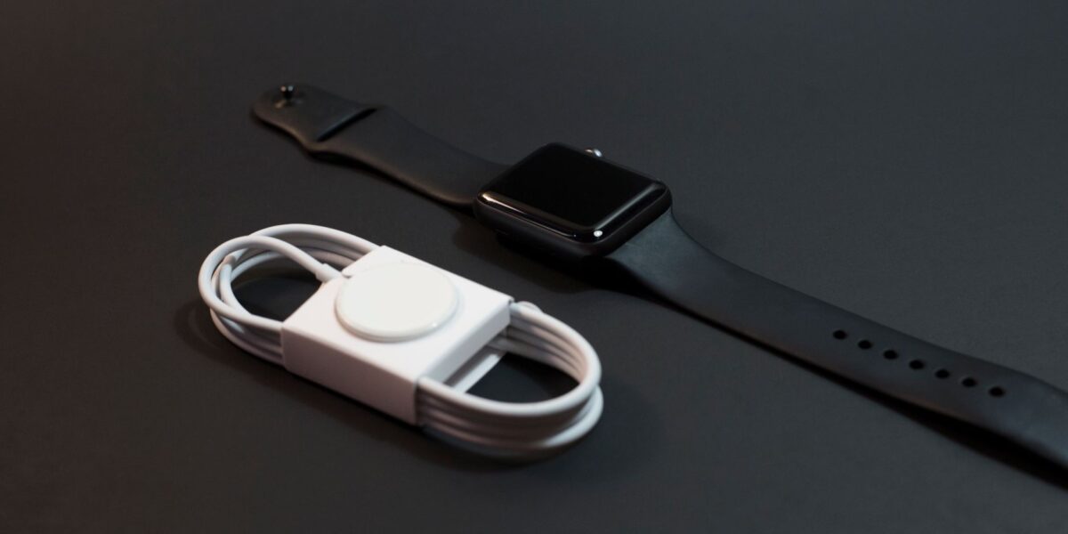 Close-up of a black smartwatch and white charging cable on a dark surface. Ideal for technology themes.
