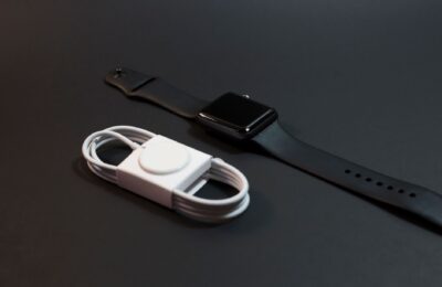 Close-up of a black smartwatch and white charging cable on a dark surface. Ideal for technology themes.