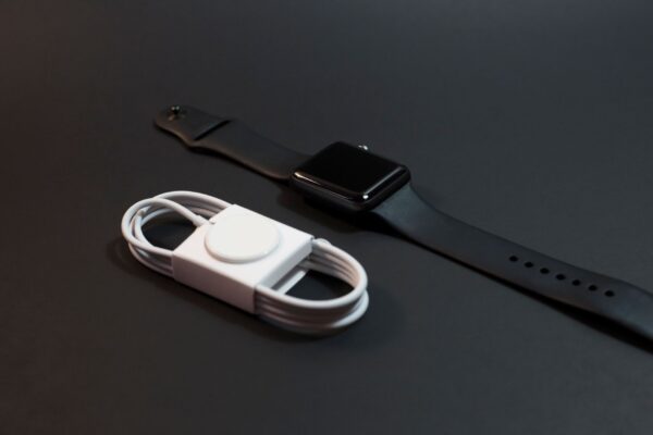 Close-up of a black smartwatch and white charging cable on a dark surface. Ideal for technology themes.