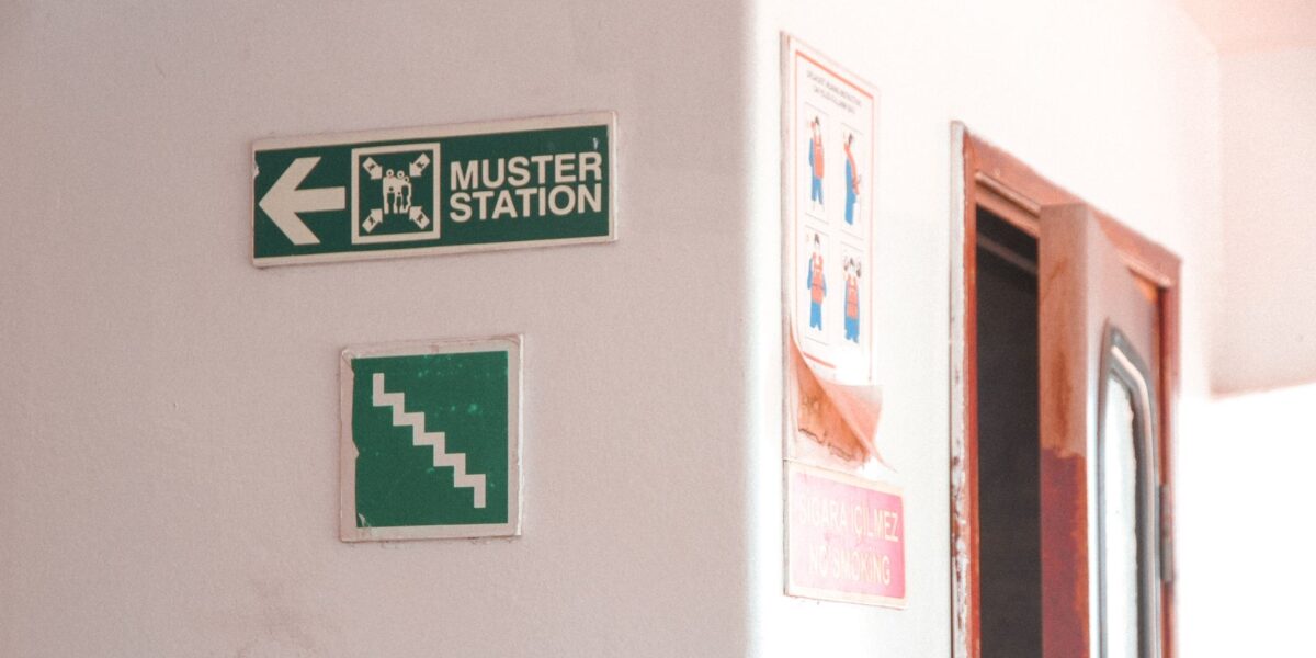 Emergency muster station signs indoors with directional and safety instructions.