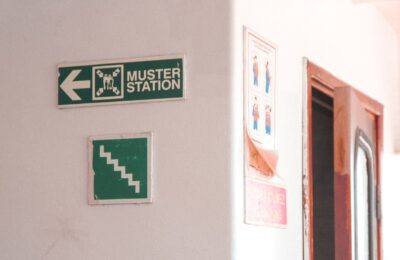 Emergency muster station signs indoors with directional and safety instructions.