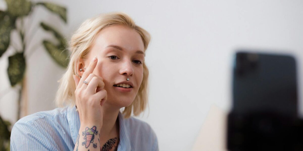 A young woman with tattoos recording a makeup tutorial with a smartphone indoors.