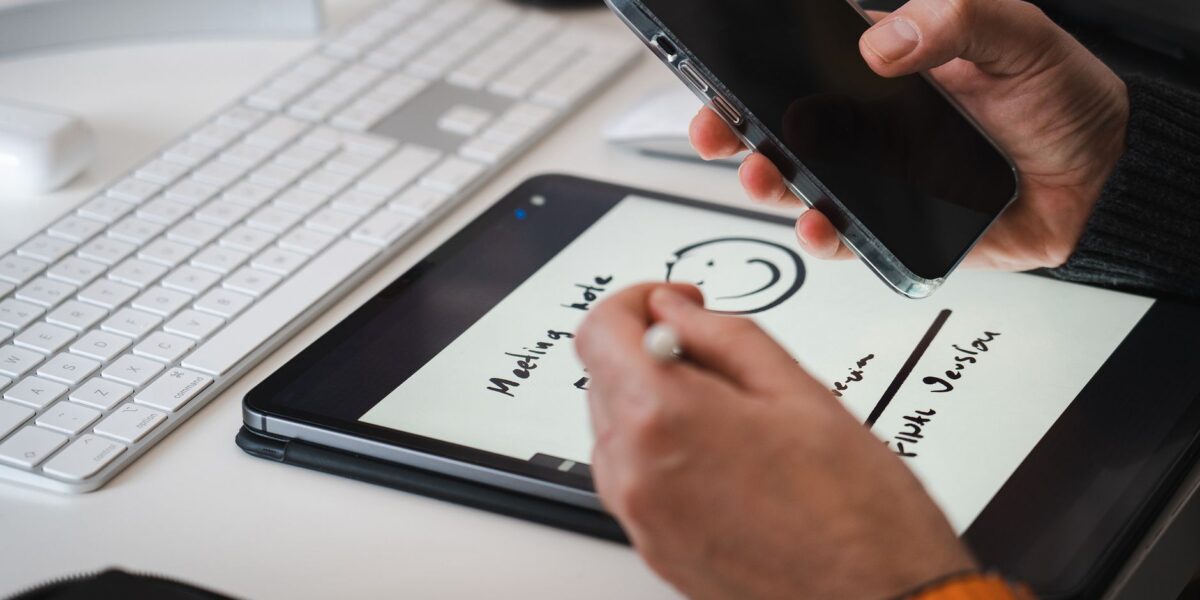 Hands using a stylus on a tablet for note-taking alongside a smartphone, suitable for tech themes.