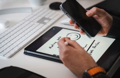 Hands using a stylus on a tablet for note-taking alongside a smartphone, suitable for tech themes.