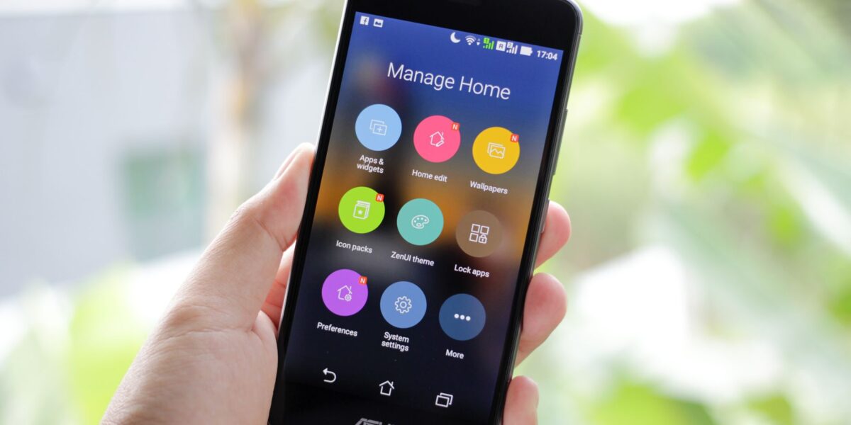 A hand holding a smartphone displaying home management apps on the screen.