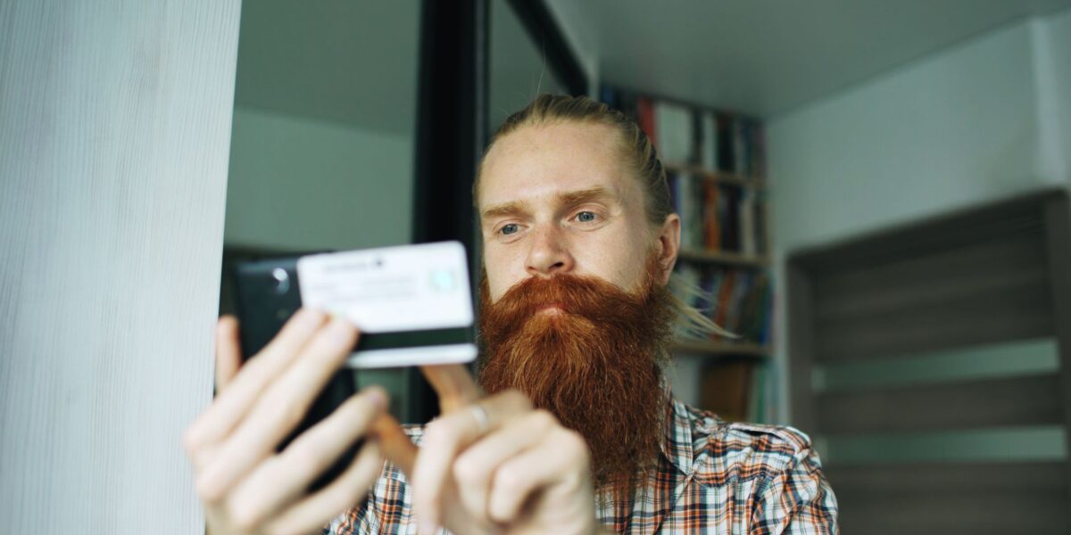 A bearded man uses his smartphone indoors, focusing on a task.