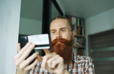 A bearded man uses his smartphone indoors, focusing on a task.