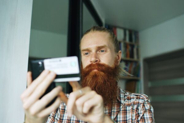 A bearded man uses his smartphone indoors, focusing on a task.