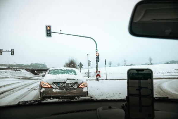 A car waits at a traffic light during snowfall on a snowy road, depicting winter driving conditions.