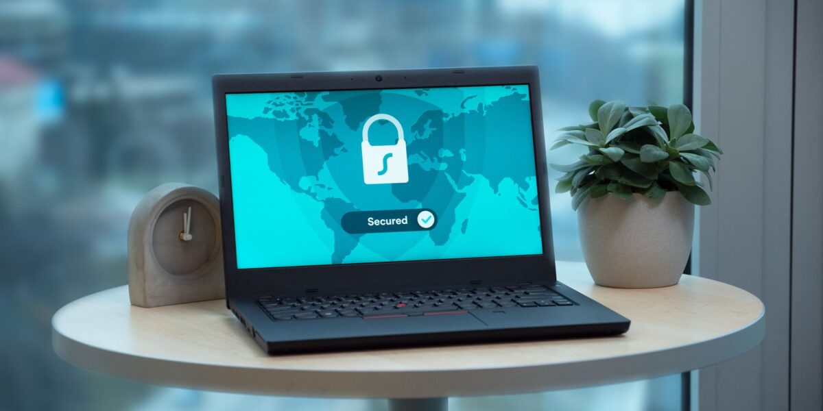 Laptop displaying a security lock icon on a table with a potted plant and clock.