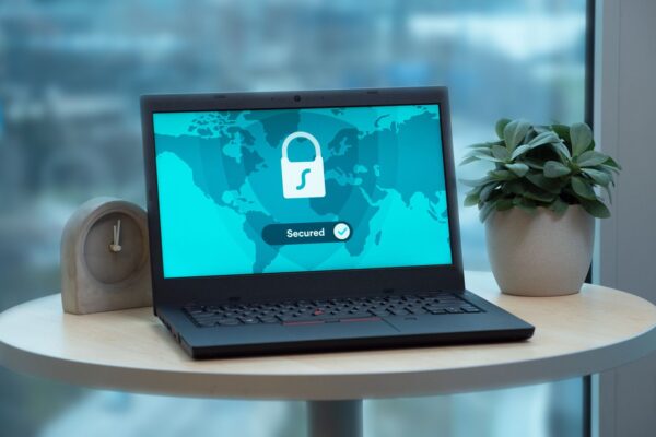 Laptop displaying a security lock icon on a table with a potted plant and clock.