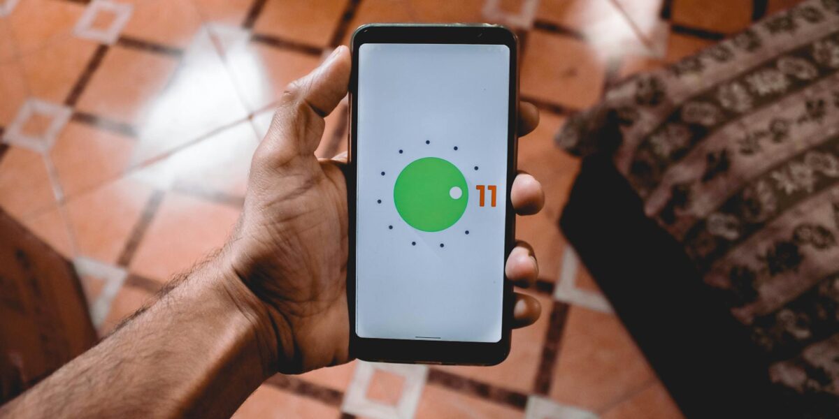 Close-up of a hand holding a smartphone displaying Android 11 interface indoors on patterned floor.