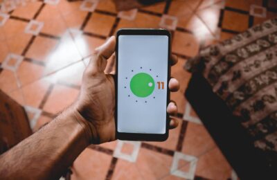 Close-up of a hand holding a smartphone displaying Android 11 interface indoors on patterned floor.