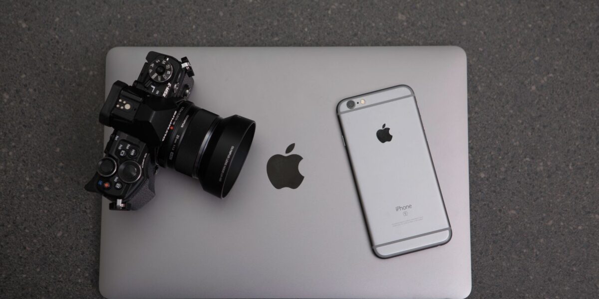 High-angle shot of DSLR camera, MacBook, and iPhone on textured surface, showcasing modern technology essentials.