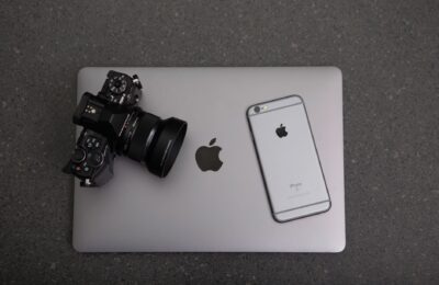 High-angle shot of DSLR camera, MacBook, and iPhone on textured surface, showcasing modern technology essentials.