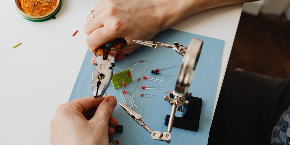 Close-up view of hands using tools to assemble electronic components with precision on a desk.