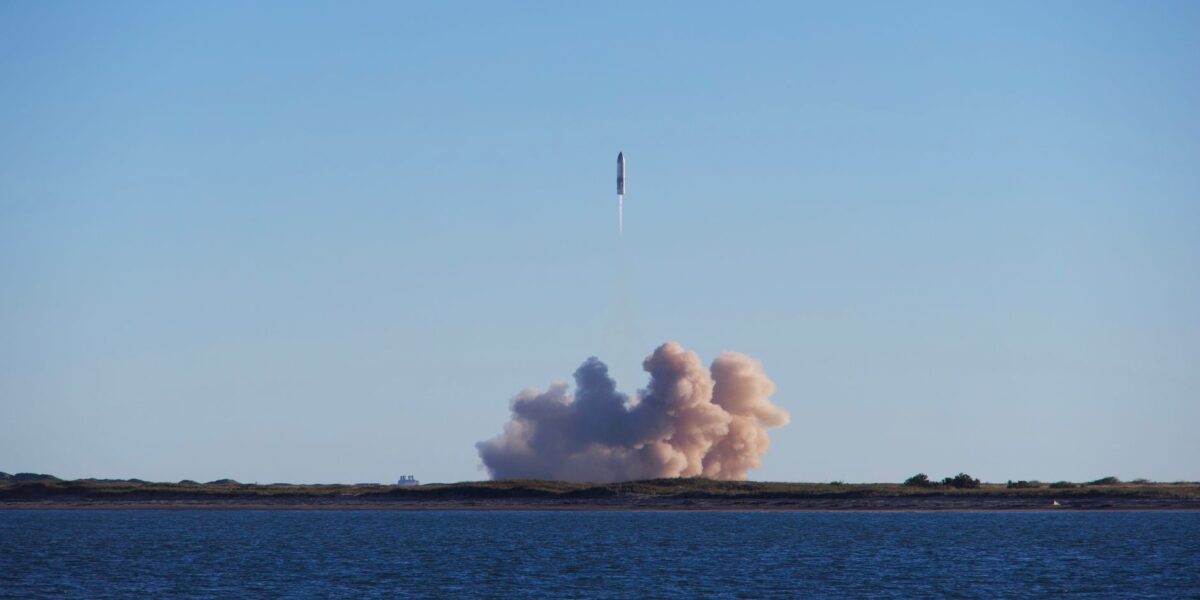 A rocket launch with smoke trails over South Padre Island, viewed across the ocean.