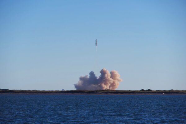 A rocket launch with smoke trails over South Padre Island, viewed across the ocean.