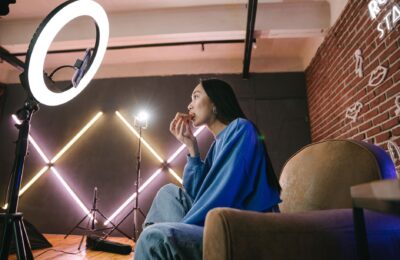 Asian woman content creator eating pizza while recording a video indoors with ring light.