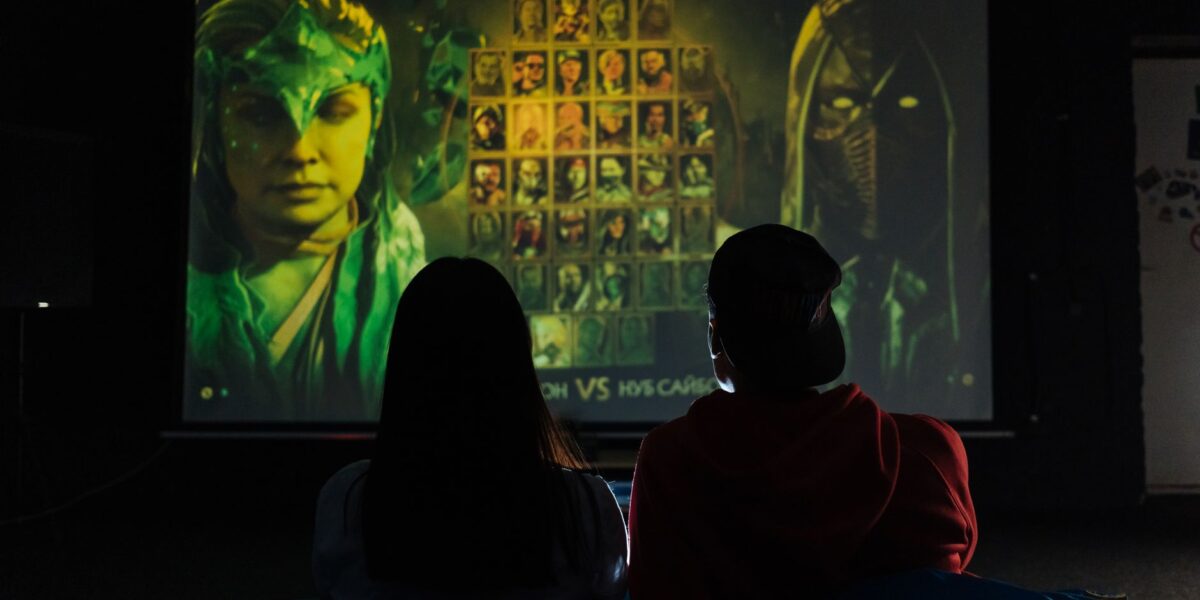 Two people sitting indoors gaming on a large projector screen, enjoying a video game session.