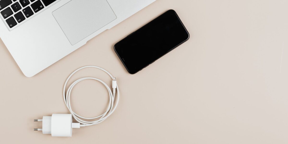 Flat lay of a laptop, smartphone, and charger on a beige background showcasing modern technology essentials.