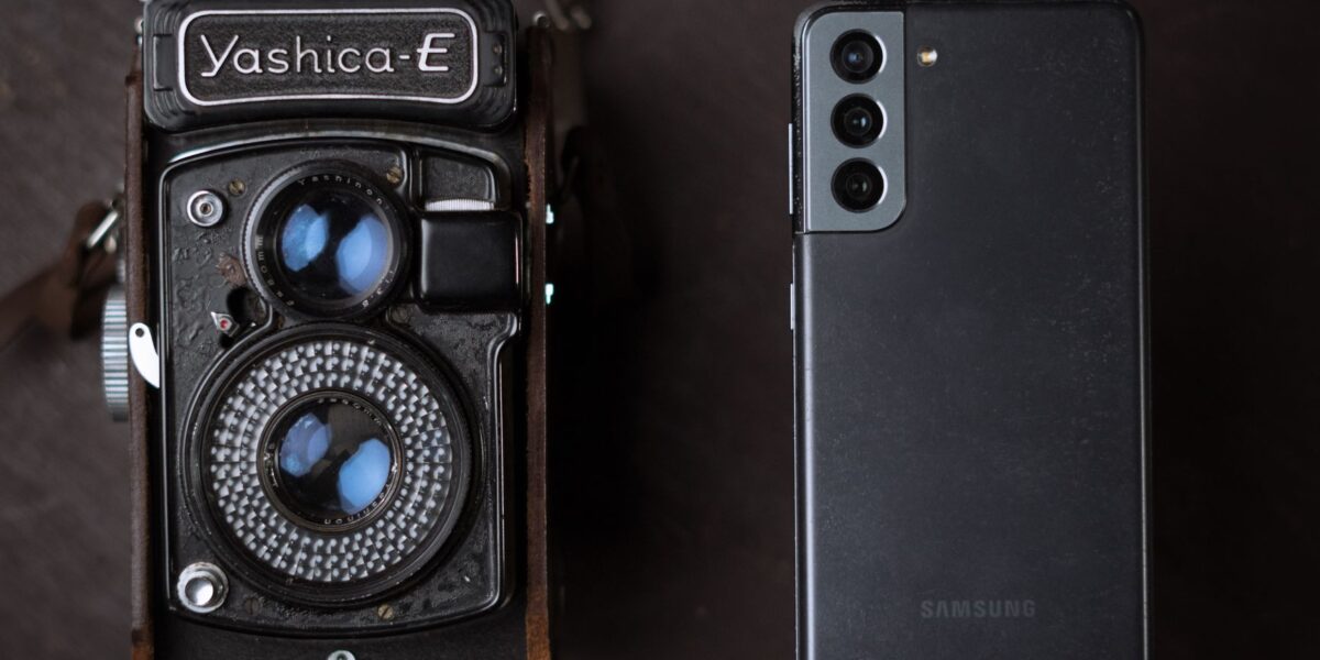 A vintage Yashica camera next to a modern smartphone, showcasing old and new technology.