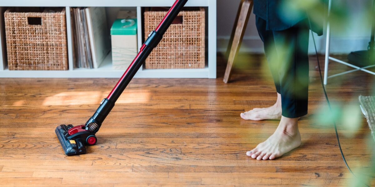 A person vacuuming wooden flooring in a cozy room, emphasizing clean living space.